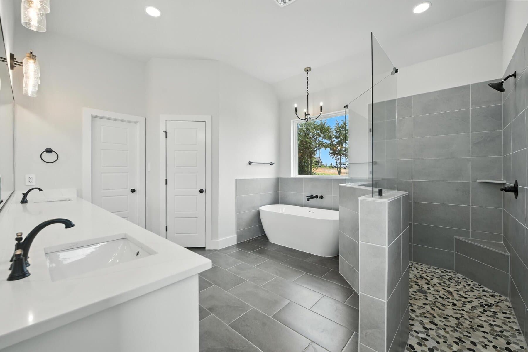 Primary bath with gray tile, freestanding tub, and walk-in shower in an Abba River Homes build.