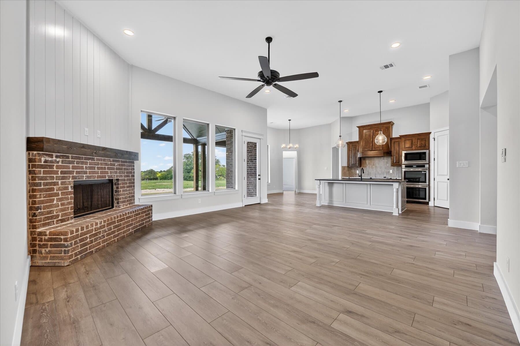 Open living room with brick fireplace, ceiling fan, and kitchen view in an Abba River Homes build.