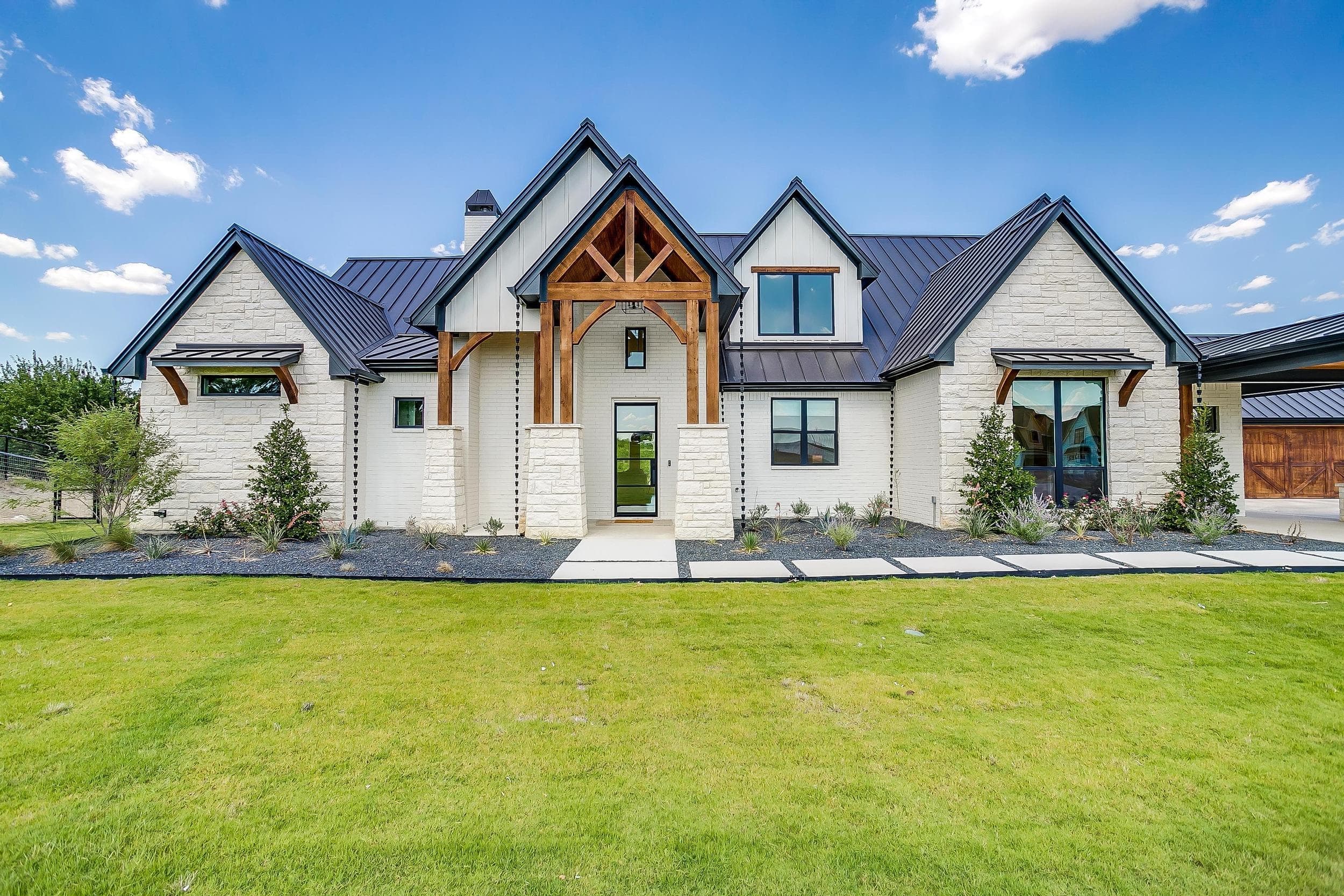 Abba River Homes exterior with white stone, brick, a timber entry, and a broad front lawn.