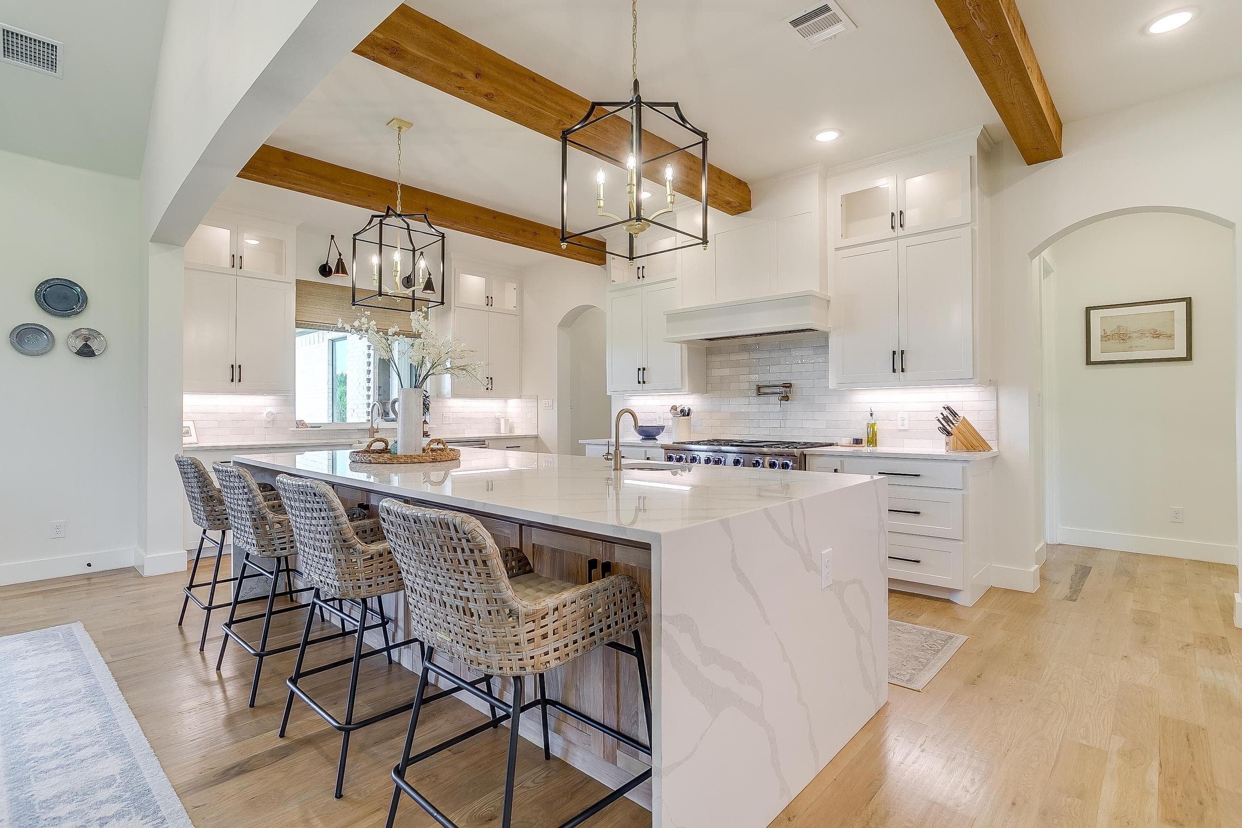 Bright Abba River Homes kitchen with an oversized island, exposed wood beams, white cabinetry, and pendant lighting.